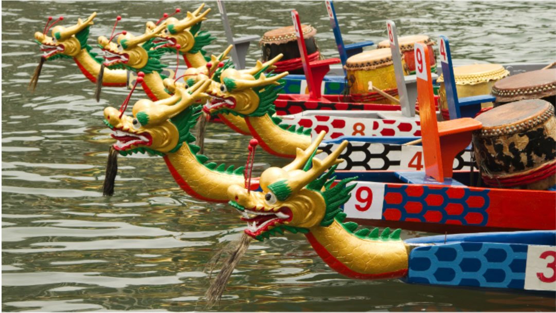 Mehrere Drachenboote mit Startnummern nebeneinander auf dem Wasser